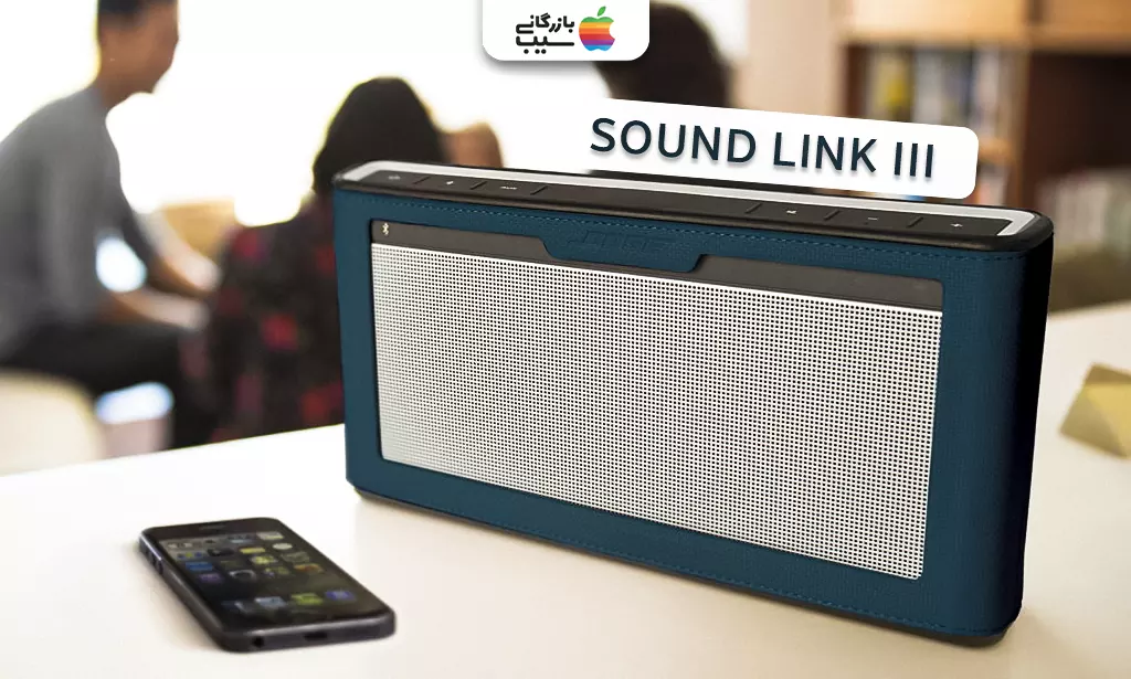 تصویری از یک اسپیکر بلوتوثی قابل حمل بوز Sound Link III به روی میز که به یک گوشی متصل است